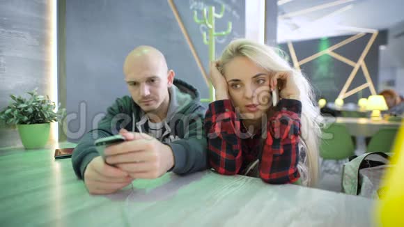 在咖啡馆的一张桌子上的男人和女人金发女孩在电话里活跃地说话她有一个重要的视频的预览图