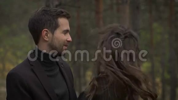 一对年轻的幸福夫妇在秋天的公园里聚在一起站在树间微笑的男人和女人视频的预览图
