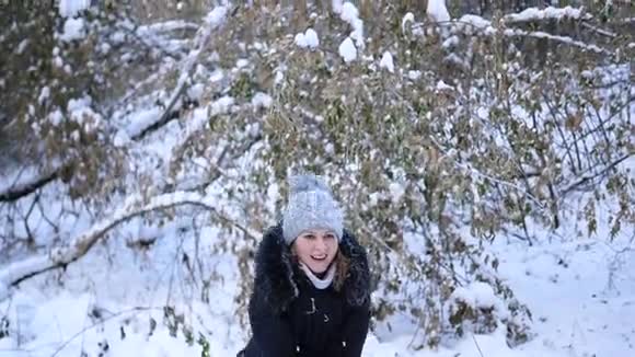 女孩把雪洒在自己身上在冬天的公园里微笑着视频的预览图