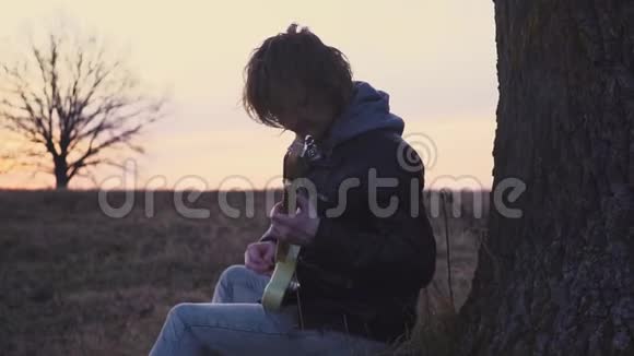 日落时分人们在树附近的田野里弹电吉他唱抒情歌曲视频的预览图