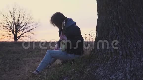 日落时分人们在树附近的田野里弹电吉他唱抒情歌曲视频的预览图