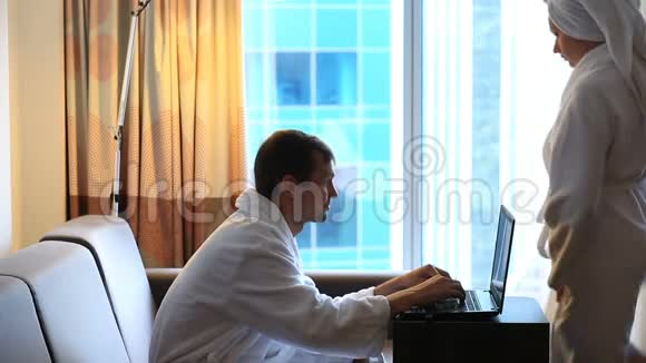 夫妻男人和女人在淋浴后坐在酒店房间的沙发上看着笔记本电脑视频的预览图