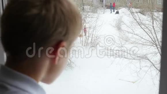 一个少年望着窗外的雪和玩耍的孩子视频的预览图