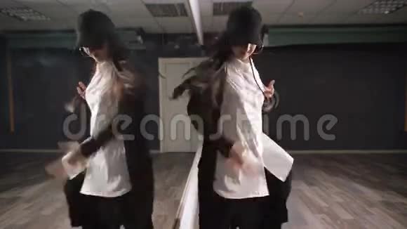 穿着白色衬衫黑色裤子和黑色帽子的长发女孩在教室附近展示了现代爵士迷舞视频的预览图