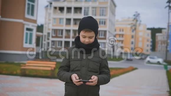 院子里站着一个男孩在街上天气很好他打扮得很暖和他穿着一件夹克一顶黑帽子和一条围巾视频的预览图