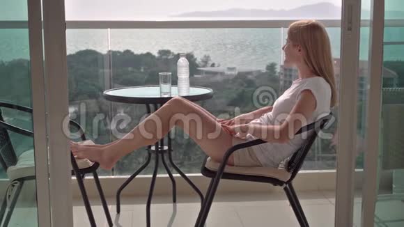 美丽迷人的女人坐在阳台的椅子上放松享受风景饮用水视频的预览图
