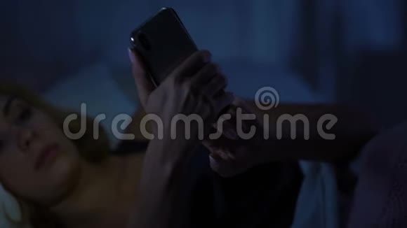 女人躺在床上在智能手机上聊天网上购物玩小玩意视频的预览图