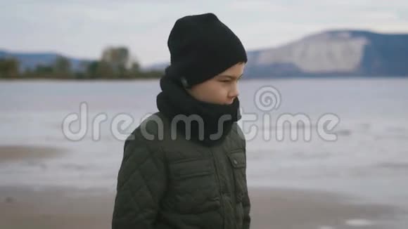 人行道一个男孩在海滩上散步他穿得很暖和他穿着一条浅色裤子和黑色靴子年轻人视频的预览图