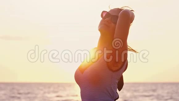 迷人的女孩戴着太阳镜长发在日落时在海滩上缓慢地摆姿势1920x1080视频的预览图