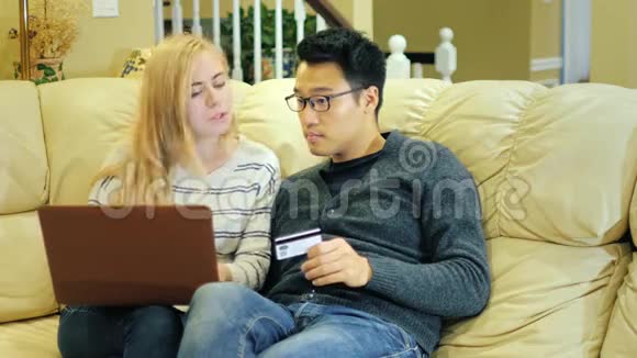 多种族夫妇在网上购物持有信用卡的亚裔男子带手提电脑的高加索女子视频的预览图