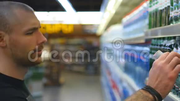 年轻人在超市里选择和购买一瓶矿泉水从杂货店货架上拿产品的家伙视频的预览图
