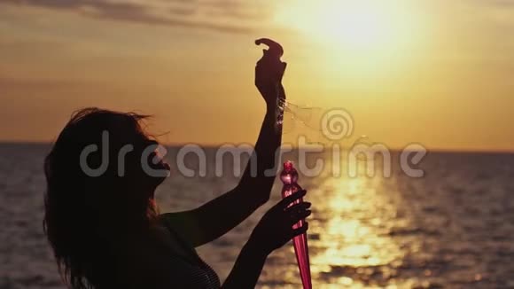 夕阳西下年轻快乐的女人在沙滩上吹着肥皂泡的剪影1920x1080视频的预览图