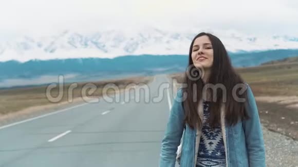 年轻女子在田野的路上搭便车年轻女孩嬉皮士在路上搭便车在山里视频的预览图
