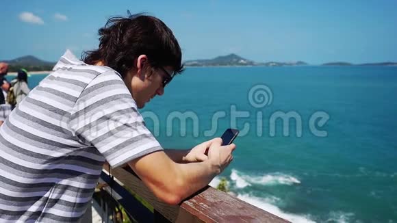 戴着太阳镜的年轻人用手机在海边发送信息慢动作1920x1080视频的预览图
