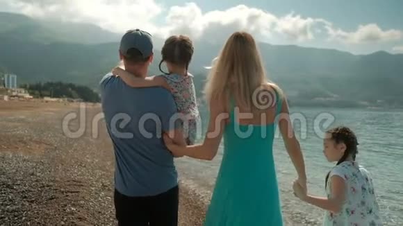 夏日带着孩子沿着海岸散步的年轻家庭视频的预览图