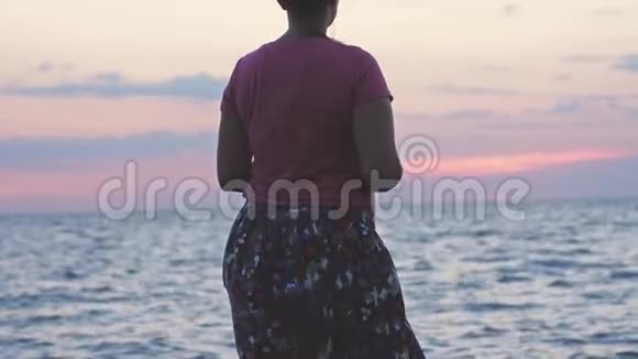 年轻女子站在岩石海滩上在日落时缓慢地享受大自然3840x2160视频的预览图