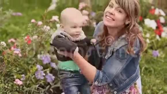 年轻漂亮的母亲正和她的小儿子坐在一片花草坪上视频的预览图