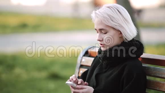 外面的金发女孩看着智能手机看着智能手机玩游戏视频的预览图