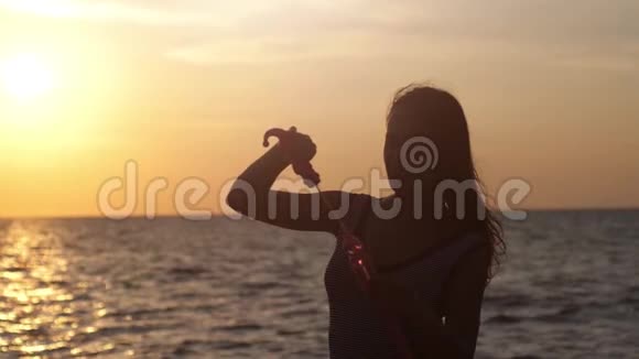快乐的黑发女孩在美丽的夕阳下在海滩上吹肥皂泡在风和日丽的天气缓慢地运动1920x1080视频的预览图