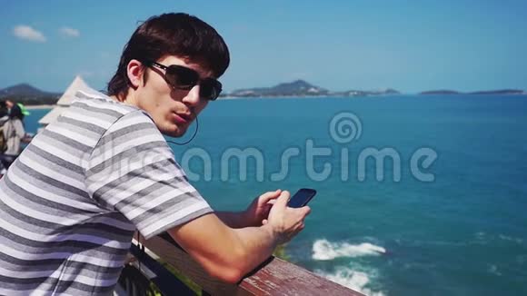 人看着相机在美丽的景色下用手机听音乐海景蓝天和清澈的地平线视频的预览图
