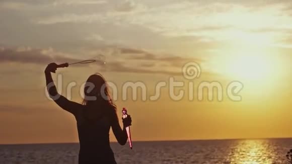 年轻快乐的女人在日落时用滑稽的方式在海滩上缓慢地吹肥皂泡1920x1080视频的预览图