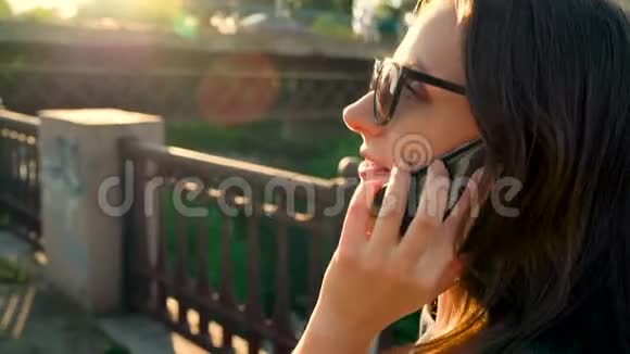 戴墨镜的女人在智能手机上说话在日落时沿着街道走特写慢动作视频的预览图