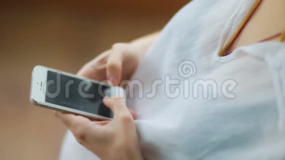 年轻孕妇在木制背景的Stadicam慢动作视频上轻敲智能手机的可爱特写视频的预览图