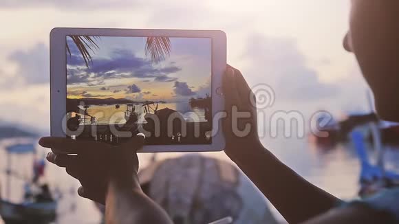 一位妇女坐在咖啡馆海滩上用一块日落的石板拍照手的特写1920x1080个视频的预览图