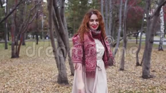 在秋天的森林里有一头红发的年轻女子在四处张望在美丽的五彩缤纷的森林里微笑视频的预览图
