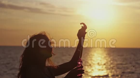 微笑的女人在美妙的夕阳下缓慢地在海滩上吹着肥皂泡1920x1080视频的预览图