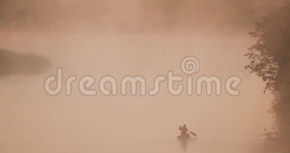 平静的湖泊河流和人钓鱼从古老的木制划船渔船在美丽的薄雾日出在夏天的早晨视频的预览图