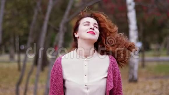 秋天的女人在秋天的森林里看着相机在美丽的五颜六色的森林树叶中微笑慢动作视频的预览图