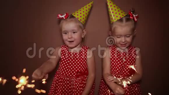 两个迷人的小妹妹双胞胎戴着节日帽手里拿着闪闪发光的孟加拉灯在假期里玩得很开心视频的预览图