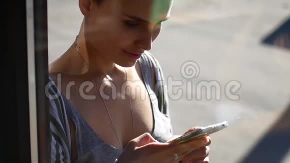 一个女孩正在看她的手机这段视频是通过咖啡馆的橱窗拍摄的女人在社交中交流视频的预览图