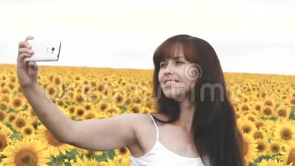 在向日葵的背景上给自己拍照的女人在网上分享你的照片视频的预览图