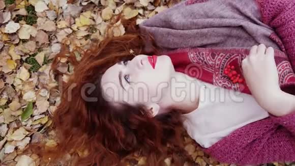 美丽的忧郁的女孩红色的头发躺在干燥的树叶上在秋天的森林中缓慢地运动3840x2160视频的预览图