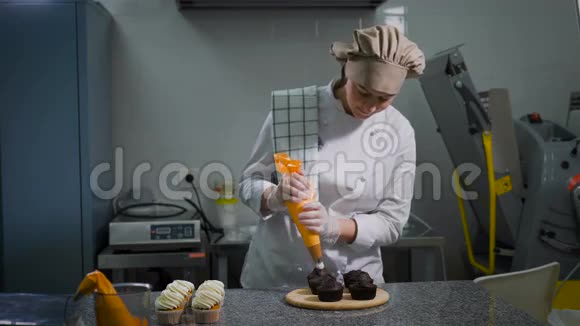 女性糕点从食品袋中轻轻挤压白色奶油牛奶奶油用于现成的巧克力纸杯蛋糕站在一个视频的预览图