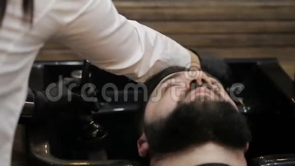 为理发做准备理发师女孩洗一个年轻人的头视频的预览图