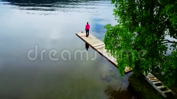 女孩在一个山湖的岸边的码头上沉思视频的预览图