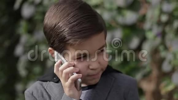穿夹克的可爱的小男孩用他的手机常春藤墙的背景视频的预览图