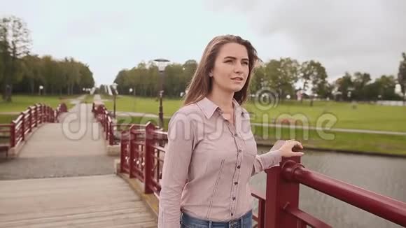年轻漂亮的女孩走在桥上穿过公园里的湖她唱这首歌视频的预览图