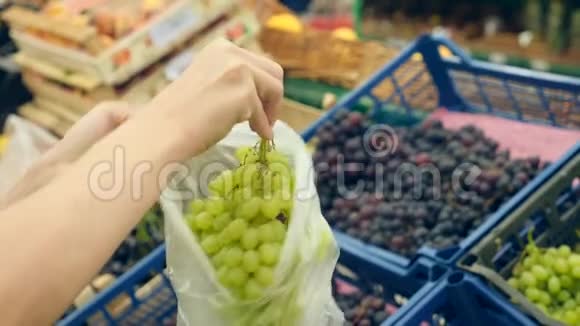 一个女人在蔬菜货架上的超市里买蔬菜和水果人选择绿葡萄慢动作4k视频的预览图