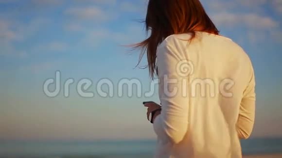 在沙滩日落时分年轻女子在你的智能手机上读留言视频的预览图