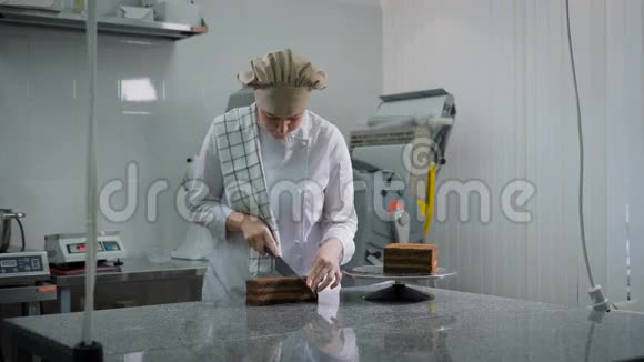 穿着白色制服的女孩在面包店的厨房里整齐地把巧克力蛋糕切成三块贝克在工作视频的预览图