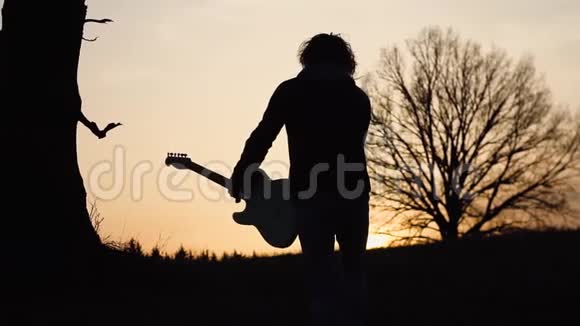 日落时分人们在靠近树的田野里弹电吉他唱抒情歌曲剪影视频的预览图