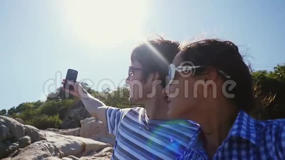 年轻夫妇在美丽的山上拍摄自拍肖像有强烈的耀斑效果背景上的太阳很慢视频的预览图