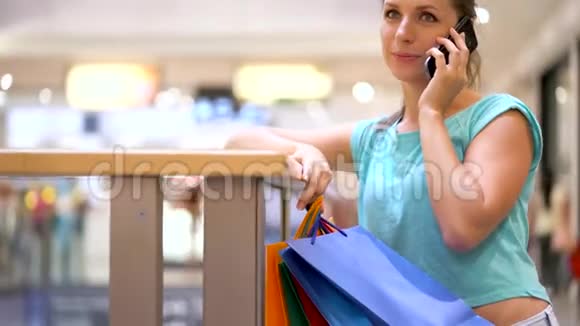 带着纸袋在购物中心的智能手机上说话的女人视频的预览图