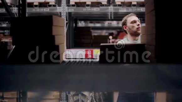 一个男人正在寻找必要的包裹从货架上拿一个在一个仓库里放着纸板箱视频的预览图