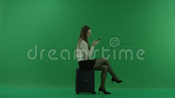 女孩看着右边坐在手提箱上看着绿色屏幕上的电话视频的预览图