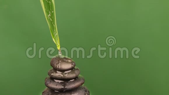 从一片绿叶上滴下的水滴落在一个由黑色石头做成的金字塔上视频的预览图